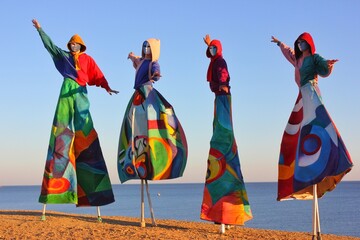 Colored theater characters in multi-colored robes and masks. The characters stand by the sea of...