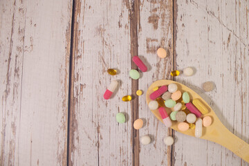 Assorted pharmaceutical medicine pills, tablets and capsules on wooden spoon.