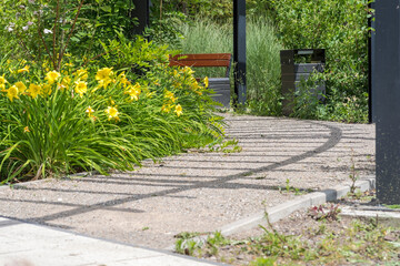 Miejskie tereny zielone. Alejka spacerowa wśród kwiatów ( jakiś gatunek lili) pod drewnianą pergolą w letnim dniu .
