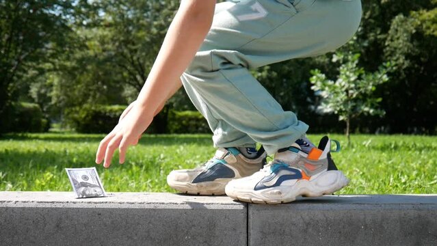 A hundred dollar bill in the park and a boy walking along the curb finds it