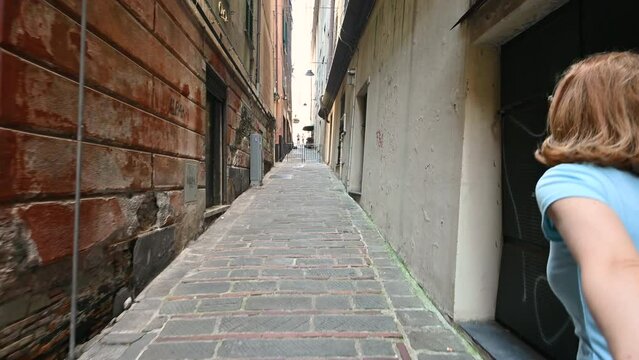 Genoa, Liguria, Italy. June 3, 2023. Engaging pov footage walking through the alleys of the historic center, a middle-aged woman precedes us who grabs our hand and leads us. Follow me concept.