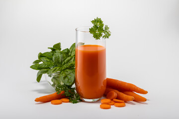 A glass of carrot juice with carrot fruits and a bunch of greens on a white background
