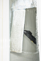 A woman washes the glass surface of the shower cabin, cleaning at home