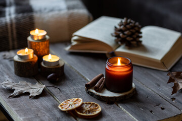 Cozy autumn or winter composition with aromatic candle, wool sweater, book. Aromatherapy, home atmosphere of cosiness and relax. Wooden background close up.
