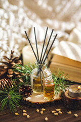 Christmas home aromatherapy. Aroma diffuser with pine extract, organic essential oil, cedar and spruce cone, candles on wooden table. Cozy atmosphere, holiday spirit. Winter inspiration and mood.