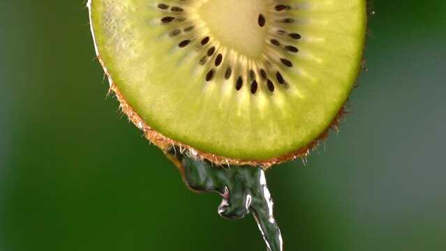 Creative mockup of sliced kiwi slice and water. Splashes on green background. Freshly chopped kiwi splashes in cold water in isolation. Concept of healthy eating and freshness. Slow motion