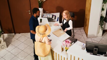 Diverse couple doing check in with receptionist, hotel concierge greeting tourists travelling on...