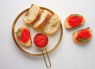 Sandwiches with red caviar and bread in a round plate on a white table, top view