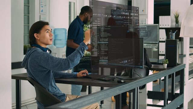 Qualified programmers helped by AR technology to visualize script in coworking space, writing code on computer using Java programming languages. Colleagues solving errors and reinforcing encryption