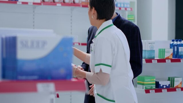 Trained pharmacy assistant helping octogenarian man with medical counsel. Elderly customer in chemist store wishing to purchase heartbeat regulating antibiotics, asking expert for guidance