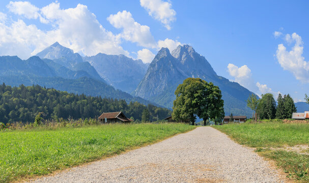 Field path near Garmisch-Partenkirchen with view to the Zugspitz massif on a sunny day with blue sky and white cumulus clouds