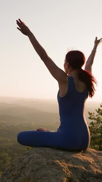 Vertical Video, Sports Girl Meditates During Sunrise. Athletic Woman Exercising in the Mountains, Sitting in Lotus Yoga Position. Healthy Lifestyle and Wellbeing, Zenism Concept. Slow Motion.