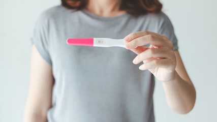 A woman holding a pregnancy test and discovering her positive result. - obrazy, fototapety, plakaty