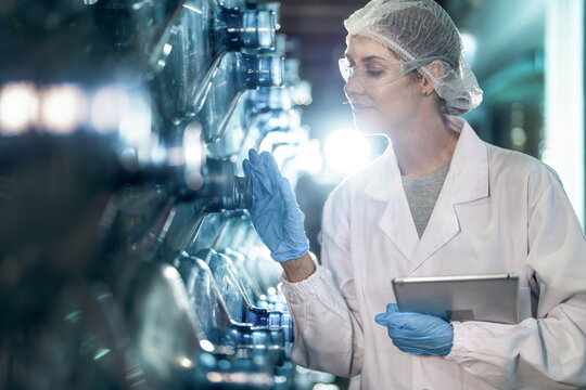 scientist worker checking the quality of water bottles on the machine conveyor line at the industrial factory. Female worker recording data at the beverages manufacturing line production.