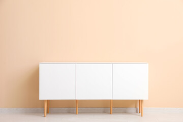 Stylish white chest of drawers near beige wall in room