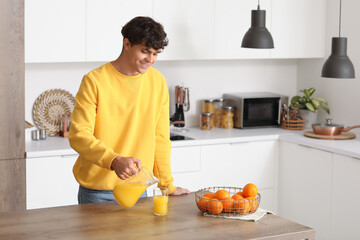 Young man pouring orange juice into glass in kitchen