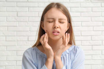 Young woman suffering from toothache on white brick background