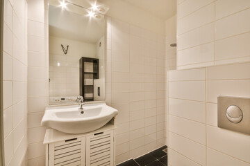 a small bathroom with white tiles and black flooring, the sink is next to the mirror on the wall