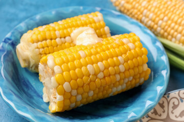 Plate of boiled corn cobs with butter on blue background, closeup
