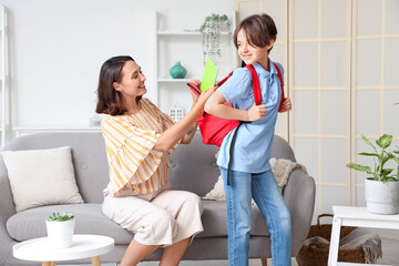 Mother putting notebooks in backpack of her little boy at home