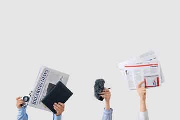 Female hands with newspapers, notebook, microphone and photo camera on light background
