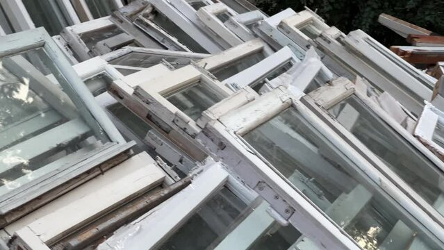 Old wooden windows lie in a pile near the building after being replaced with modern double-glazed windows