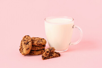 Cup of milk and tasty cookies with chocolate chips on pink background