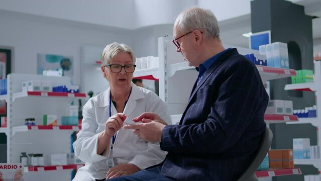 Elderly pharmacist in drugstore with senior patient after finishing annual examination, suggesting him medical products to treat illness symptoms. Older man receiving treatment from specialist