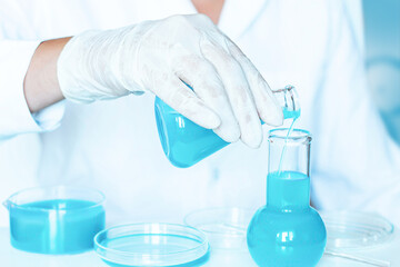 Scientific Setup: Lab Aide Transfers Flask's Contents, Blue Fluid, to Bottle. White Lab Coat. Glass Instruments.