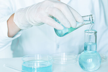 In the lab: Liquid is poured into flasks by an assistant wearing a white lab coat and gloves. Glass...