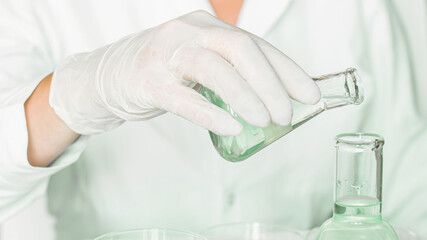 Lab backdrop: Assistant performs tasks in the laboratory environment. Adorned in lab coat. Dominant green hues. Employing glass apparatus. Green laboratory focused on plant research.