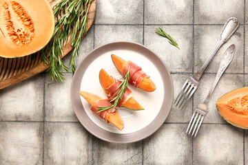Plate of delicious melon with prosciutto and rosemary on grey tile background - Powered by Adobe
