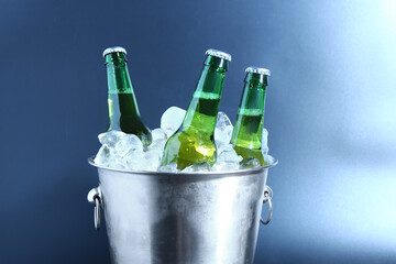 Bucket with bottles of cold beer and ice cubes on color background