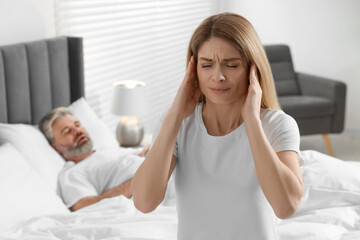 Irritated woman covering her ears in bed at home. Problem with snoring husband