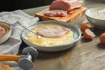 Cooking schnitzel. Raw pork chop in eggs, meat mallet and ingredients on wooden table