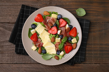 Tasty salad with brie cheese, prosciutto, almonds and berries on wooden table, top view