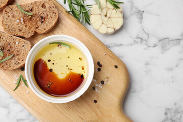 Bowl of organic balsamic vinegar with oil, bread slices and spices on white marble table, flat lay. Space for text