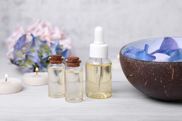 Spa composition. Bottles of essential oil and aromatic water with flowers in bowl on white wooden table, closeup