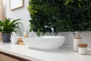 Green artificial plants, vessel sink and different personal care products in bathroom