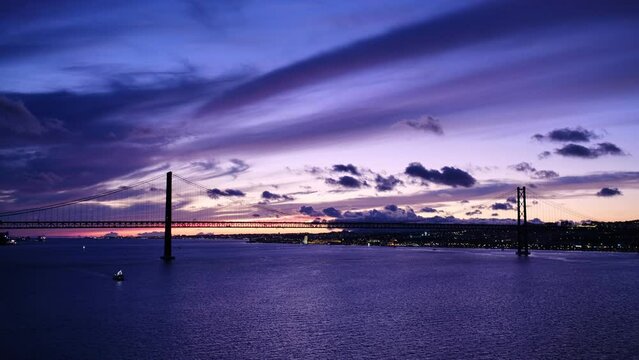 View of 25 de Abril Bridge famous tourist landmark of Lisbon connecting Lisboa and Almada on Setubal Peninsula over Tagus river in the evening twilight with boats. Lisbon, Portugal