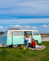 couple doing a road trip with an old vintage car in the Dutch flower bulb region with tulip fields during Spring in the Netherlands, camper van with picnic in front