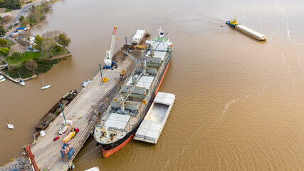 Self unloading bulk carrier cargo hatches open unloading sugar. Sugar is loaded onto barges and trucks. Aerial front view.