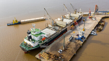 Self unloading bulk carrier cargo hatches open unloading sugar. Sugar is loaded onto barges and trucks. Aerial stern view.