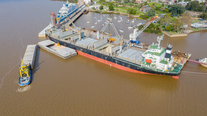 Self unloading bulk carrier cargo hatches open unloading sugar. Sugar is loaded onto barges and trucks. Aerial side view.