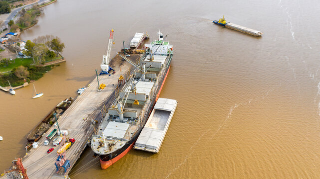 Self unloading bulk carrier cargo hatches open unloading sugar. Sugar is loaded onto barges and trucks. Aerial front view.