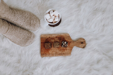 Female legs in warm socks near cup of hot marshmallow chocolate and brownies cake on wooden tray on...