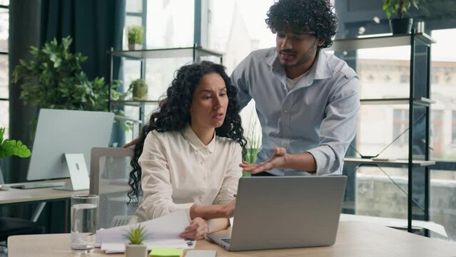 Arabian man business coach helping Hispanic woman intern businessman mentor consult colleague businesswoman teaching explain e-commerce data get shock result online job work laptop cooperate in office