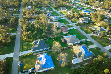 Aerial view of damaged in hurricane Ian houses roofs covered with blue protective tarp against rain...