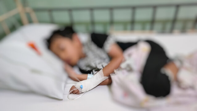 Blurry image of a sick boy sleeping in a hospital bed with an IV in hand