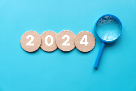 New year 2024 concept. Magnifying glass with a wooden circle with number over a blue background.